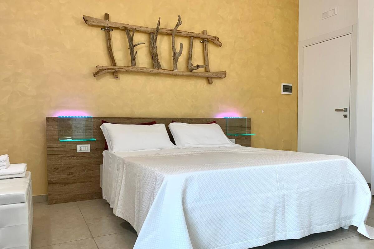 Une chambre à coucher comprenant un lit, des tables de chevet, une œuvre d’art murale en bois et une porte.