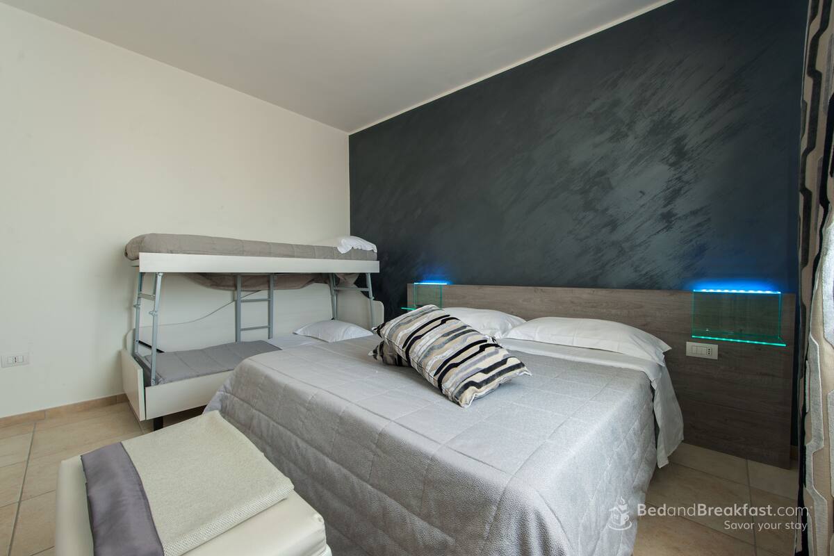 Une chambre moderne avec un lit superposé, deux lits simples, une table de chevet avec une lampe et un luminaire fixé au mur.