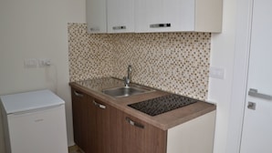 Een compacte keuken met een ingebouwd spoelbakje, houten kastjes en een betegelde spatwand.