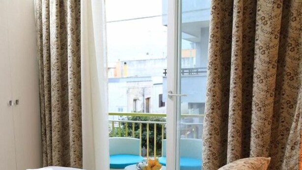 Een hotelkamer met een bed, een balkon met een blauwe stoel en gordijnen met een patroon.
