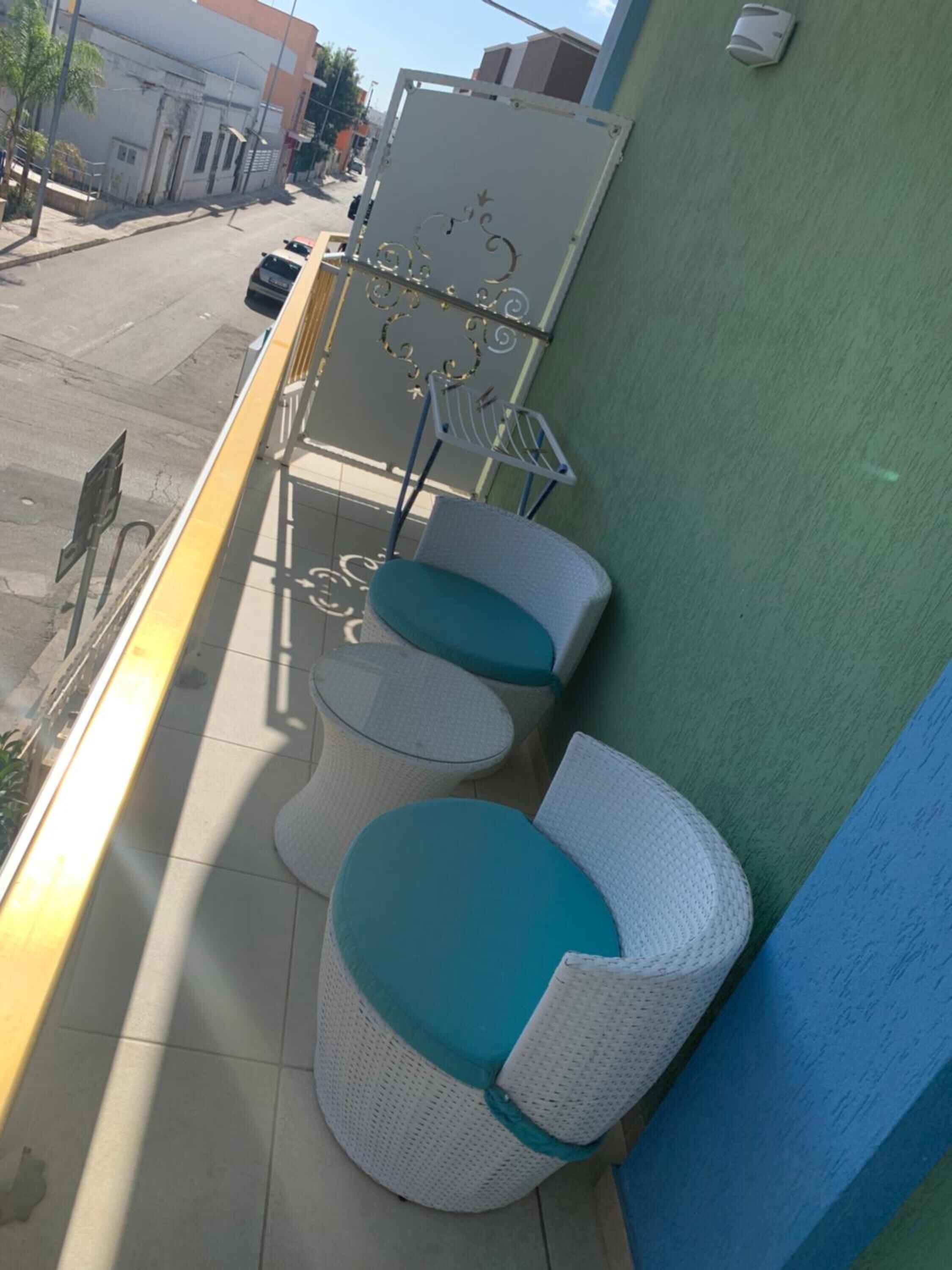 A balcony with two wicker chairs and a small table, a metal gate, and a street view.