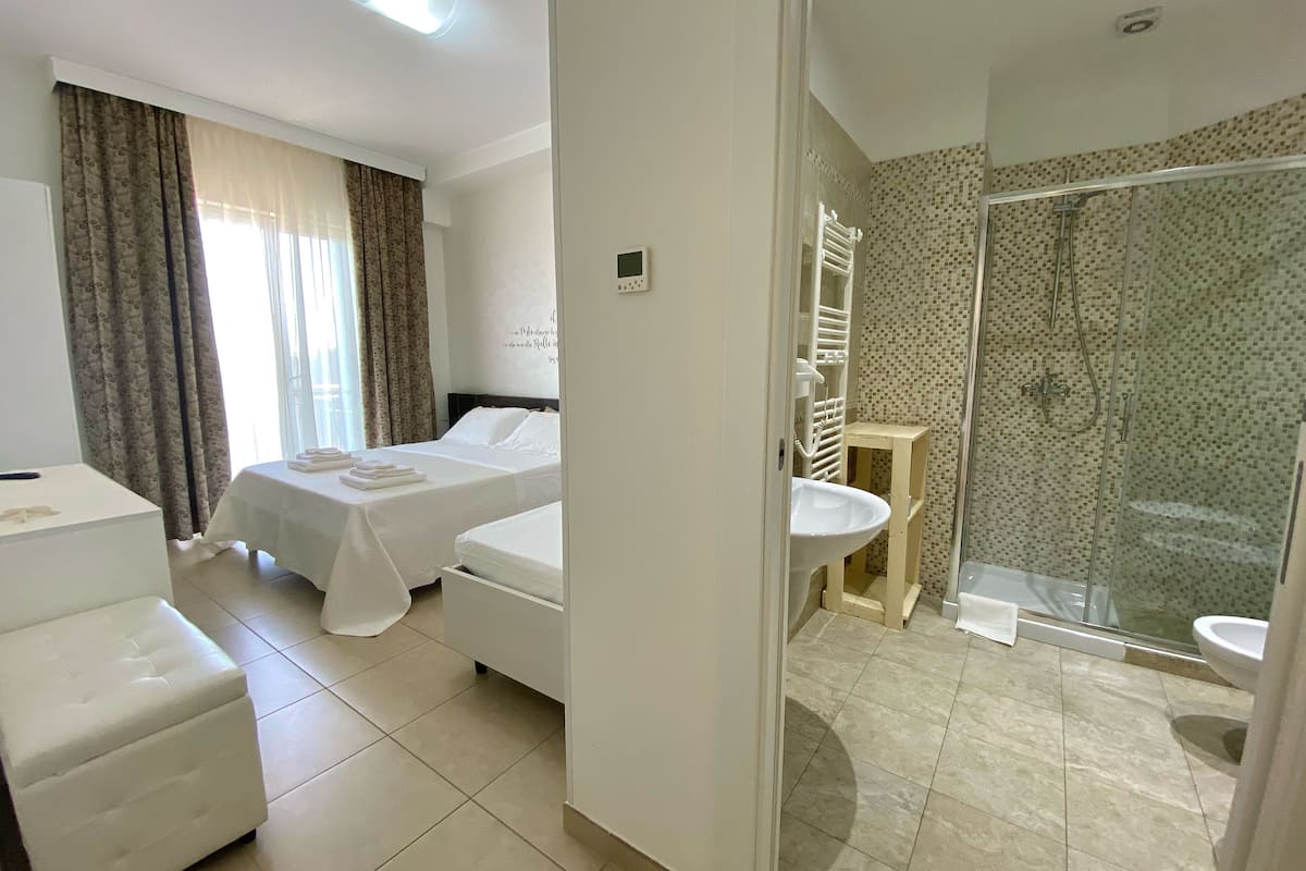 Une chambre d’hôtel avec deux lits, un canapé, une salle de bain avec douche et un lavabo.