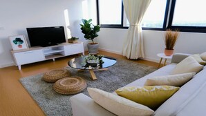 A modern living room with a flat-screen TV, a sofa, a coffee table, and two potted plants.