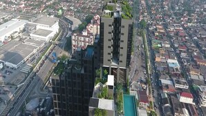 A high-rise building with a modern design, surrounded by a dense urban area with various other buildings.