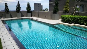 A rectangular swimming pool with a tiled floor, surrounded by a low concrete wall and a grassy area.