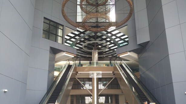 A modern interior with two escalators, a central column, and a decorative ceiling structure.