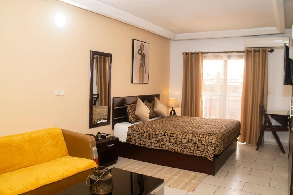 Habitación de hotel con cama, sofá, escritorio, silla, televisión y ventana con cortinas.