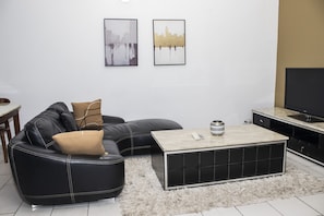 A modern living room with a black leather sectional sofa, a light-colored coffee table, and a flat-screen TV on a stand.