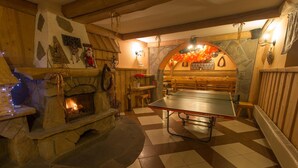 A cozy room with a stone fireplace, a ping pong table, and a stone wall with a decorative archway. - Tatrzański Dworek (Bialy Dunajec)
