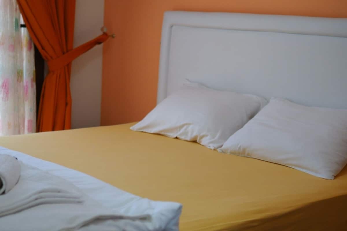 A bed with a white headboard and two white pillows, a yellow bedspread, and a white shirt on the bed.