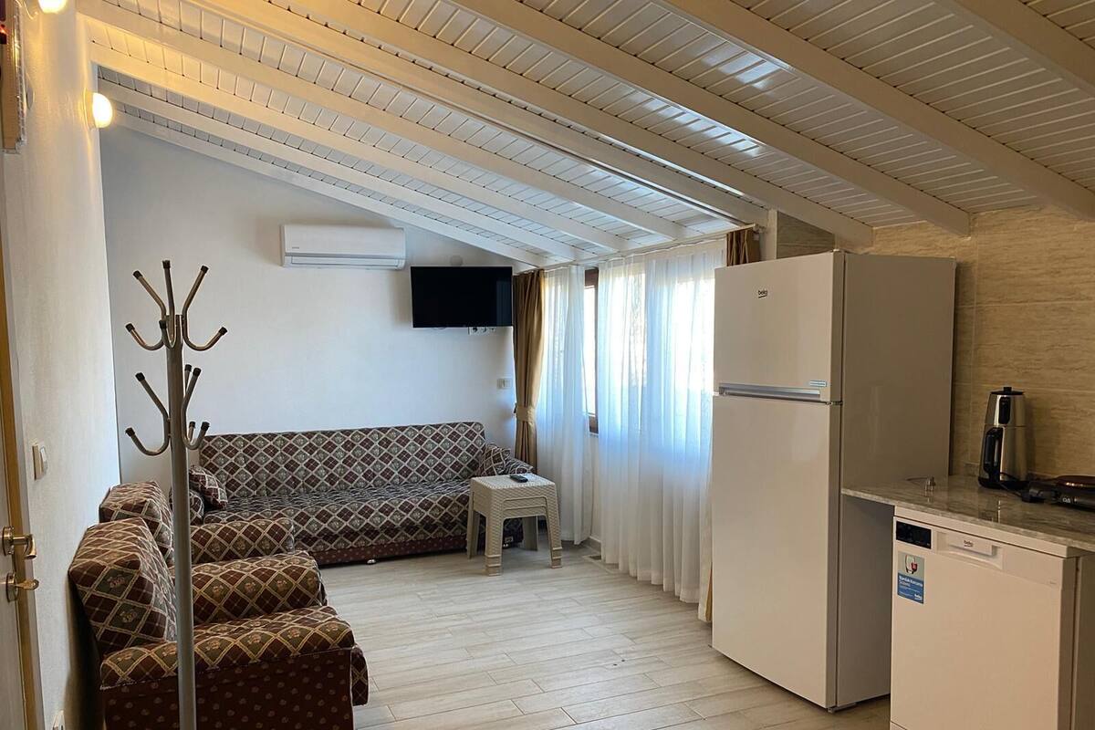 A compact living space with a sofa, a small table, a coat rack, a refrigerator, and a coffee maker.