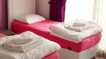 Duas camas com roupa de cama rosa e branca, uma cabeceira branca e uma cortina roxa.