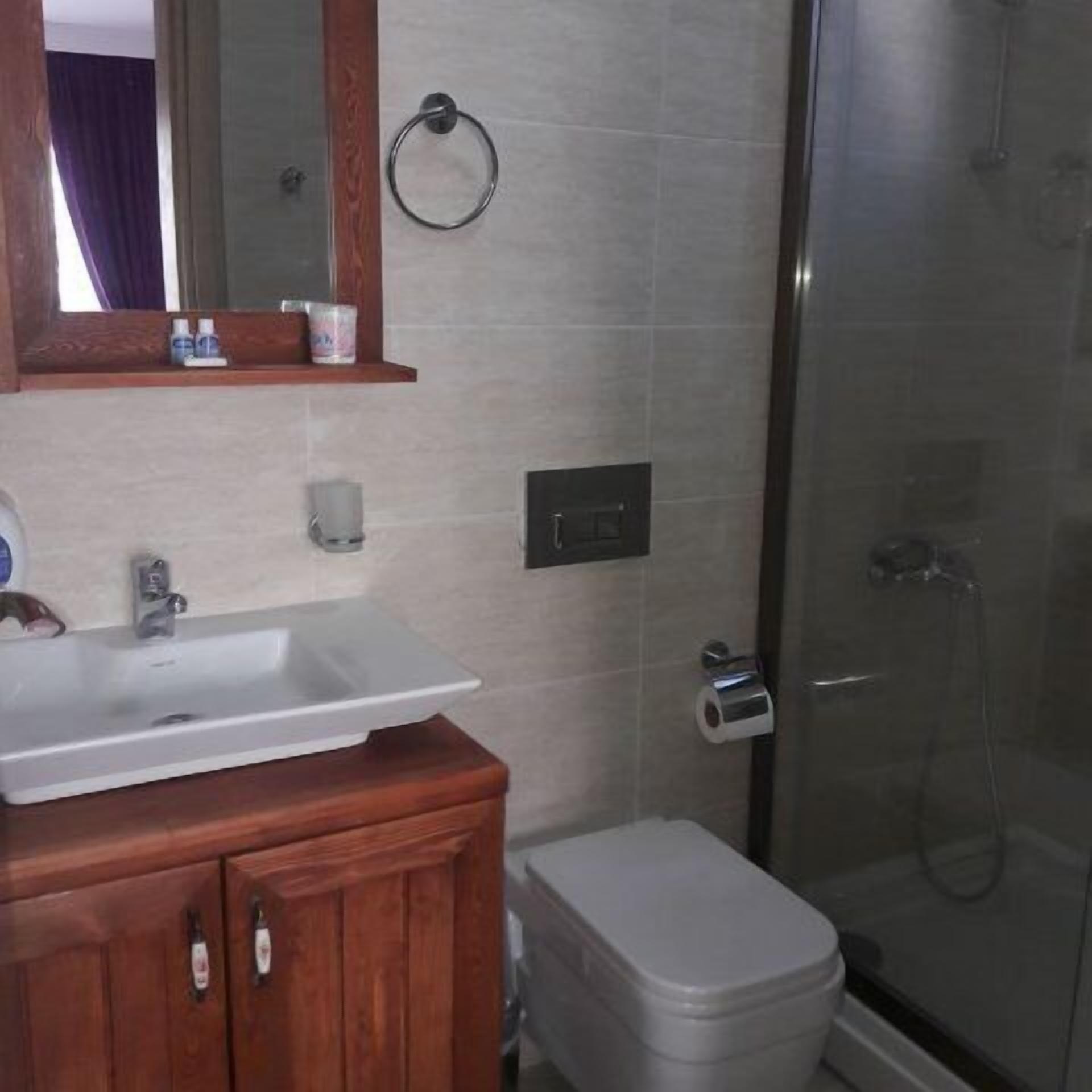 A bathroom with a wooden vanity, a white sink, a mirror, a towel ring, a toilet, and a glass-enclosed shower.