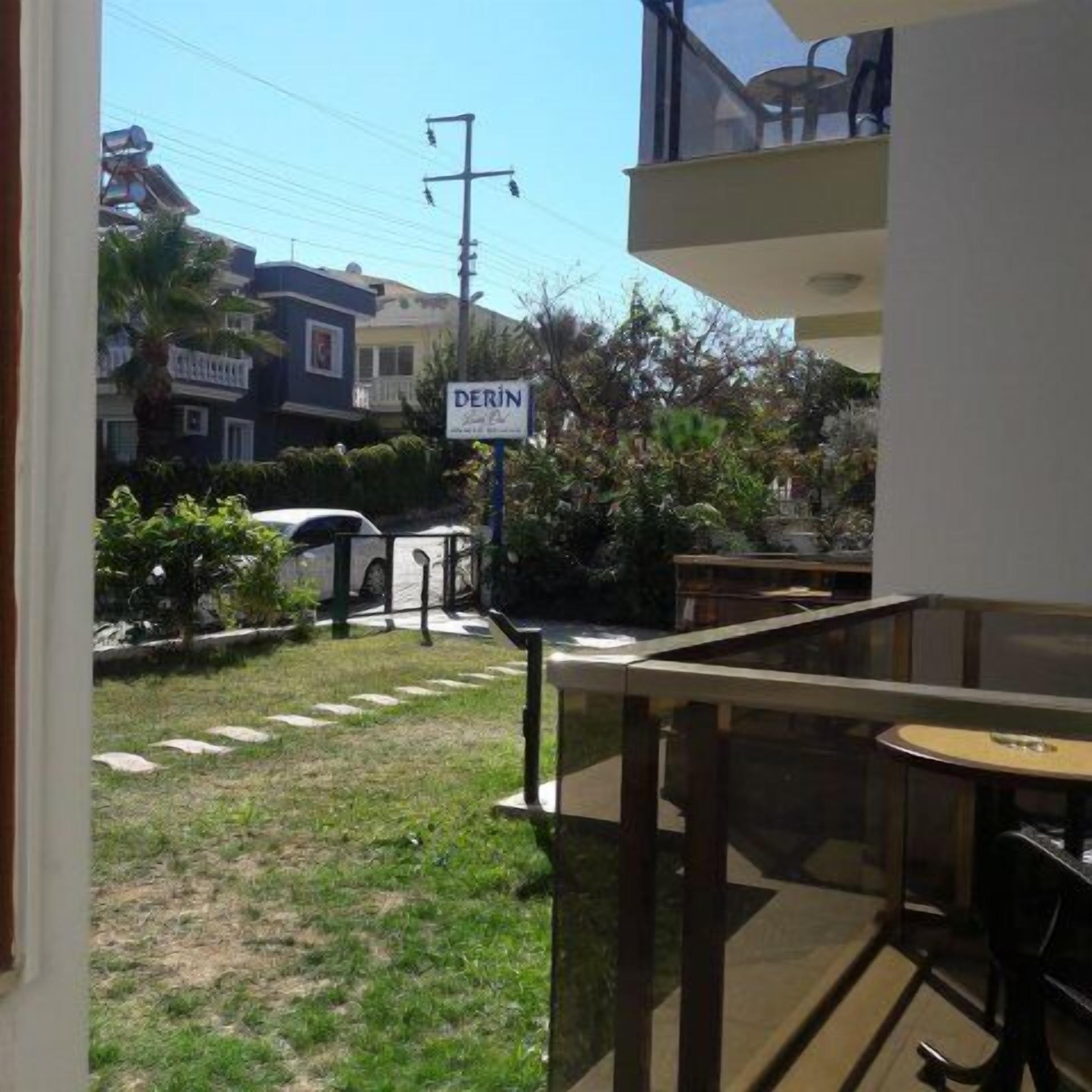 A balcony with a table and chairs, a sign reading "DERIN," and a view of a residential area with houses and a parked car.