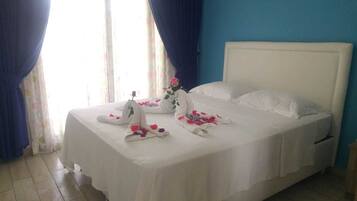 A neatly made bed with white linens, a single rose on the pillow, and a bouquet of flowers on the nightstand.