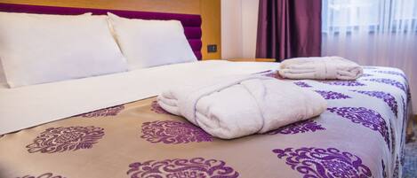 A neatly made bed with a purple and white patterned bedspread, a wooden headboard, and a pair of folded towels on the bed.