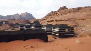 A desert landscape with several black and white striped tents. - Wadi Rum Firecamp (Wadi Rum)