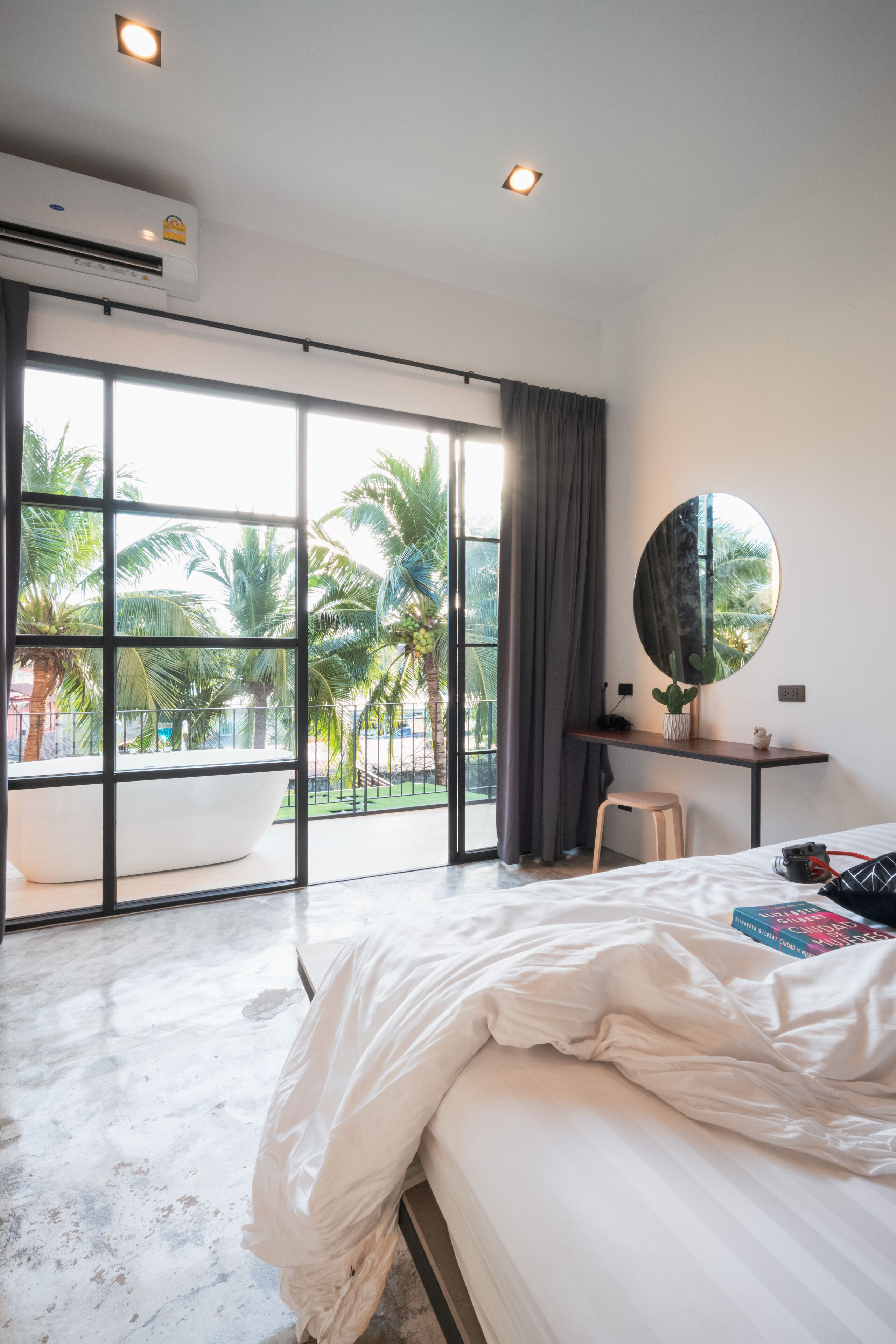 Une chambre moderne avec une grande fenêtre, un lit, un bureau et un miroir rond.