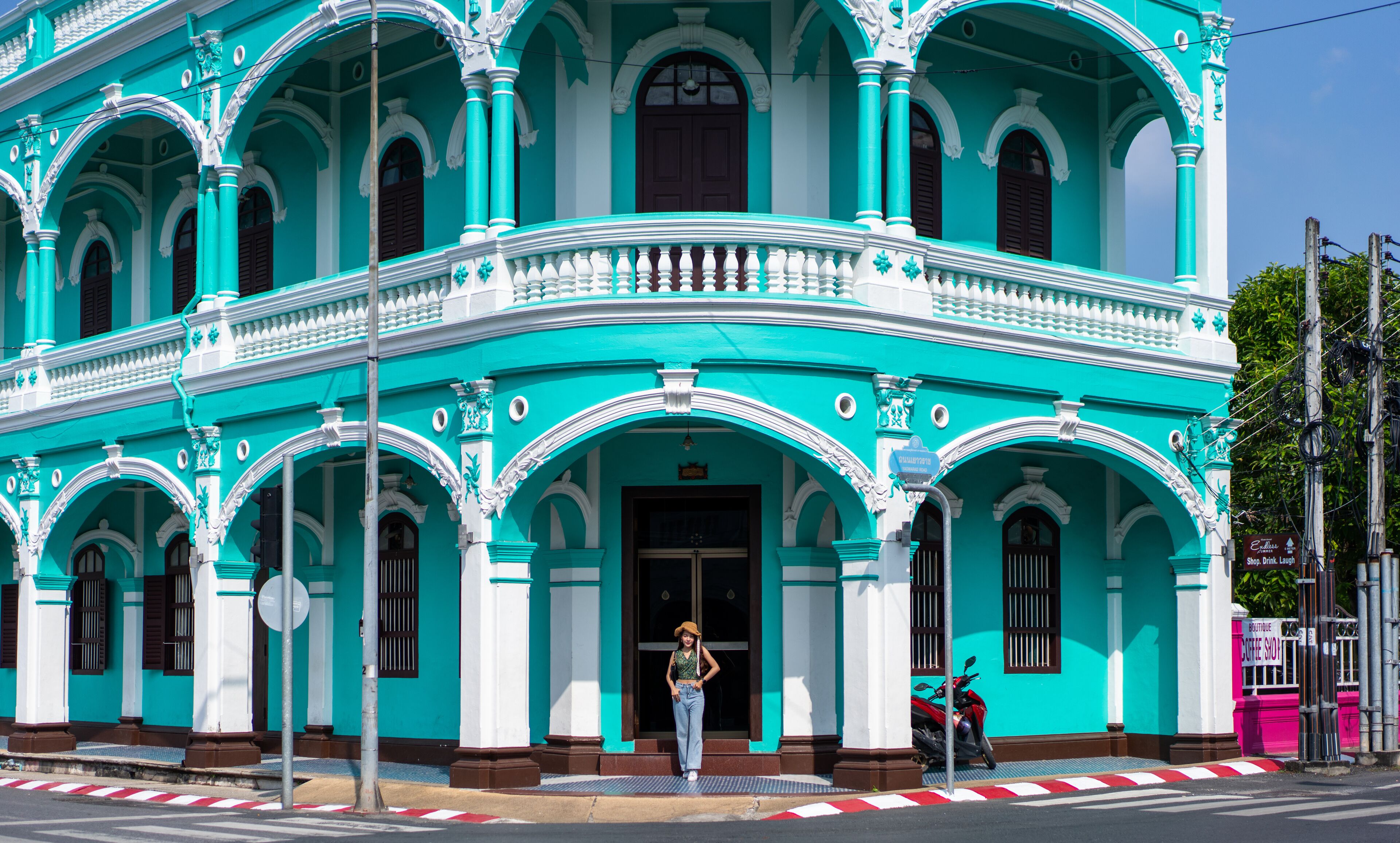 A turquoise colonial-style building with a balcony, a sign for a coffee shop, and a parked motorcycle.
