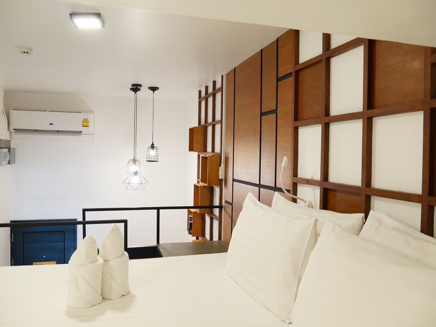 A hotel room with a bed, white pillows, a wooden headboard, and pendant lights.