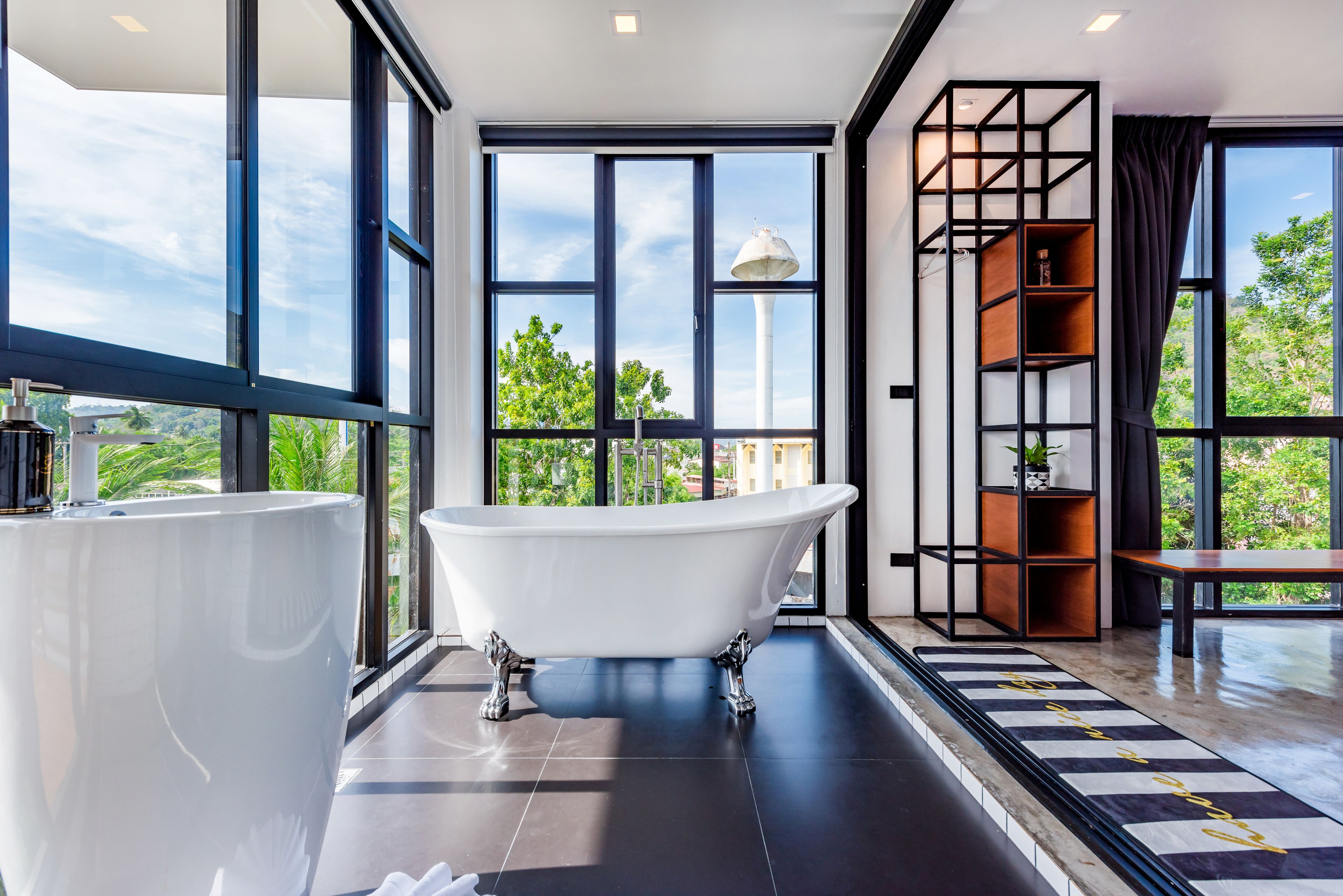 Un baño moderno con una bañera independiente, ventanas amplias y vistas a la vegetación.