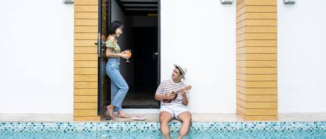 Zona de piscina con suelo de baldosas, pared de madera y una persona sentada junto a la piscina.