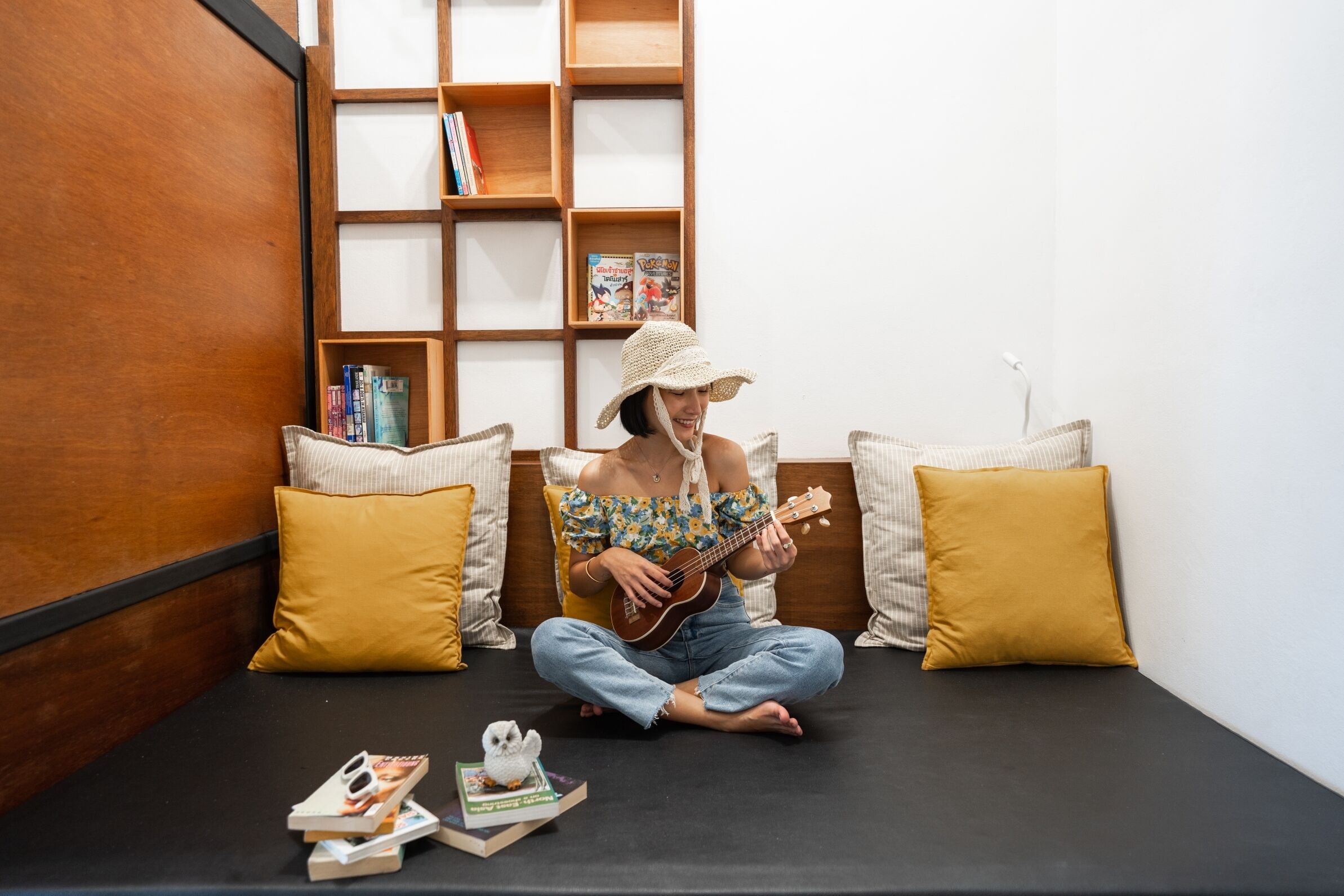 A person sitting on a black sofa in a room with wooden shelves and yellow pillows.