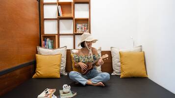 A person sitting on a black sofa in a room with wooden shelves and yellow pillows.