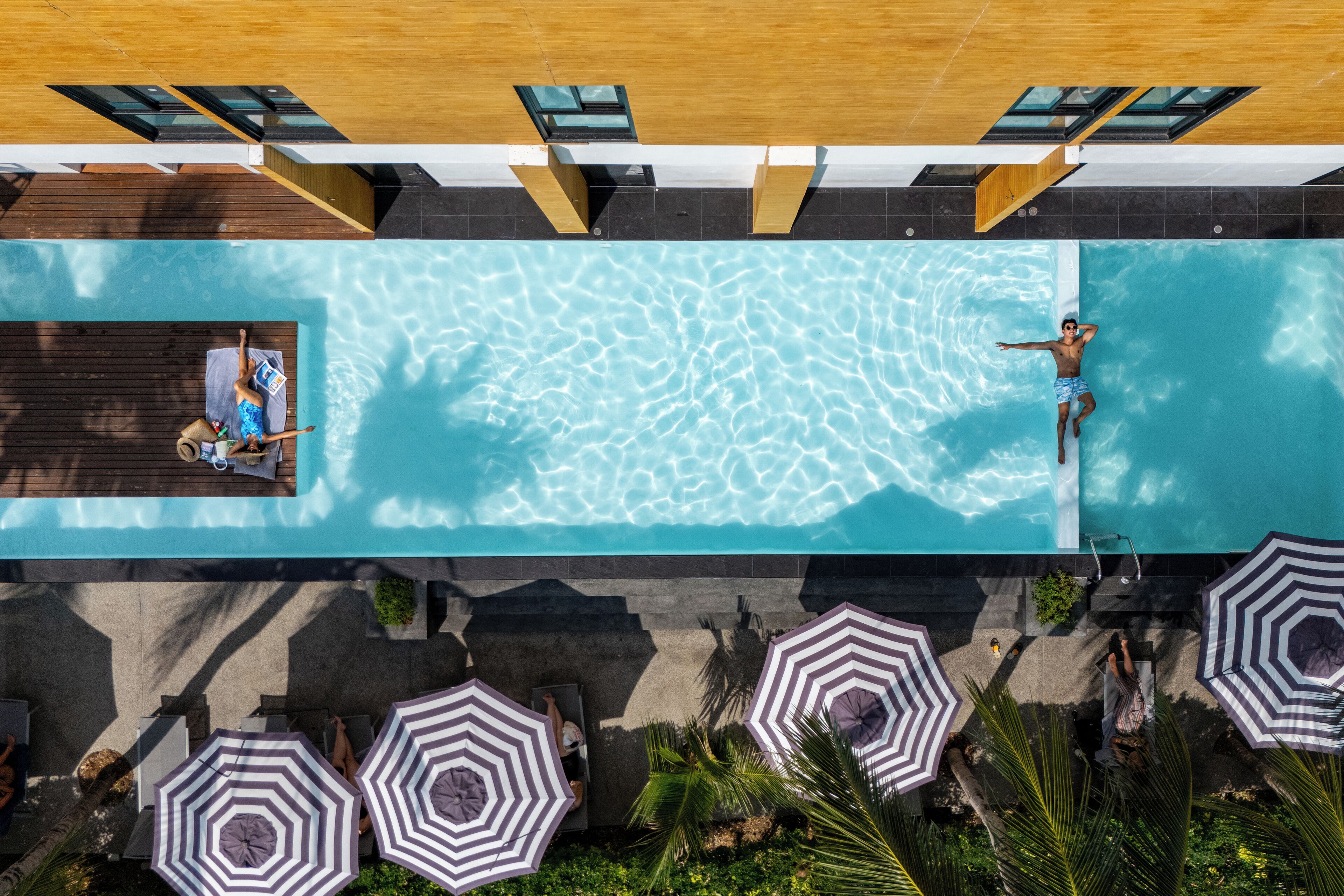 An aerial view of a swimming pool with a wooden deck, lounge chairs, and umbrellas.