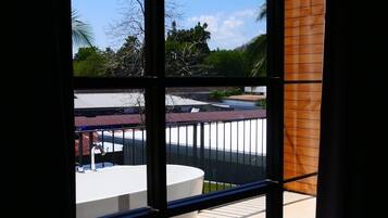 Un baño moderno con una bañera grande, un ventanal con vistas a una piscina y zona exterior, y una toalla en el suelo.