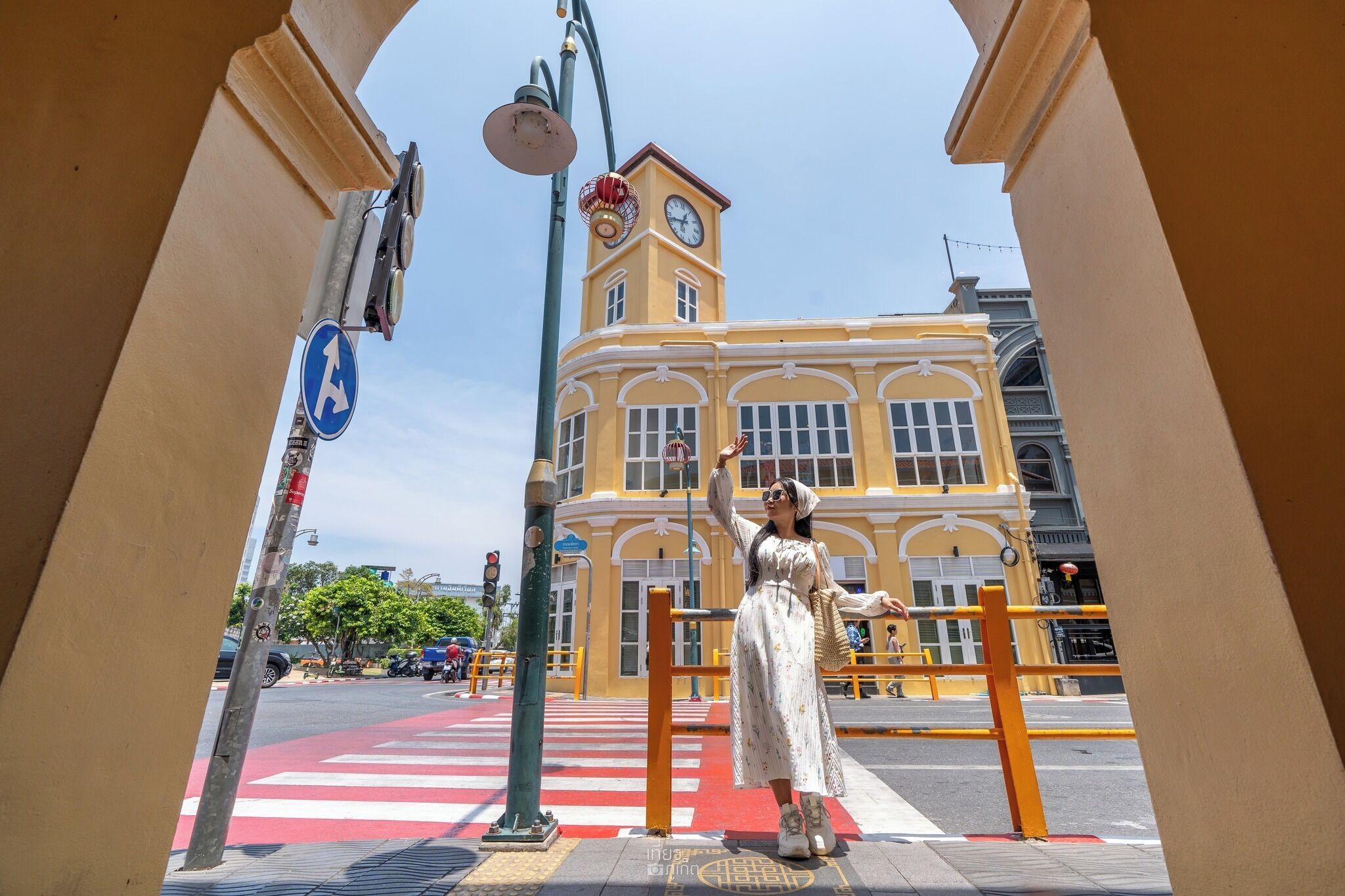 A yellow building with a clock tower, a pedestrian crossing, and a street with vehicles.