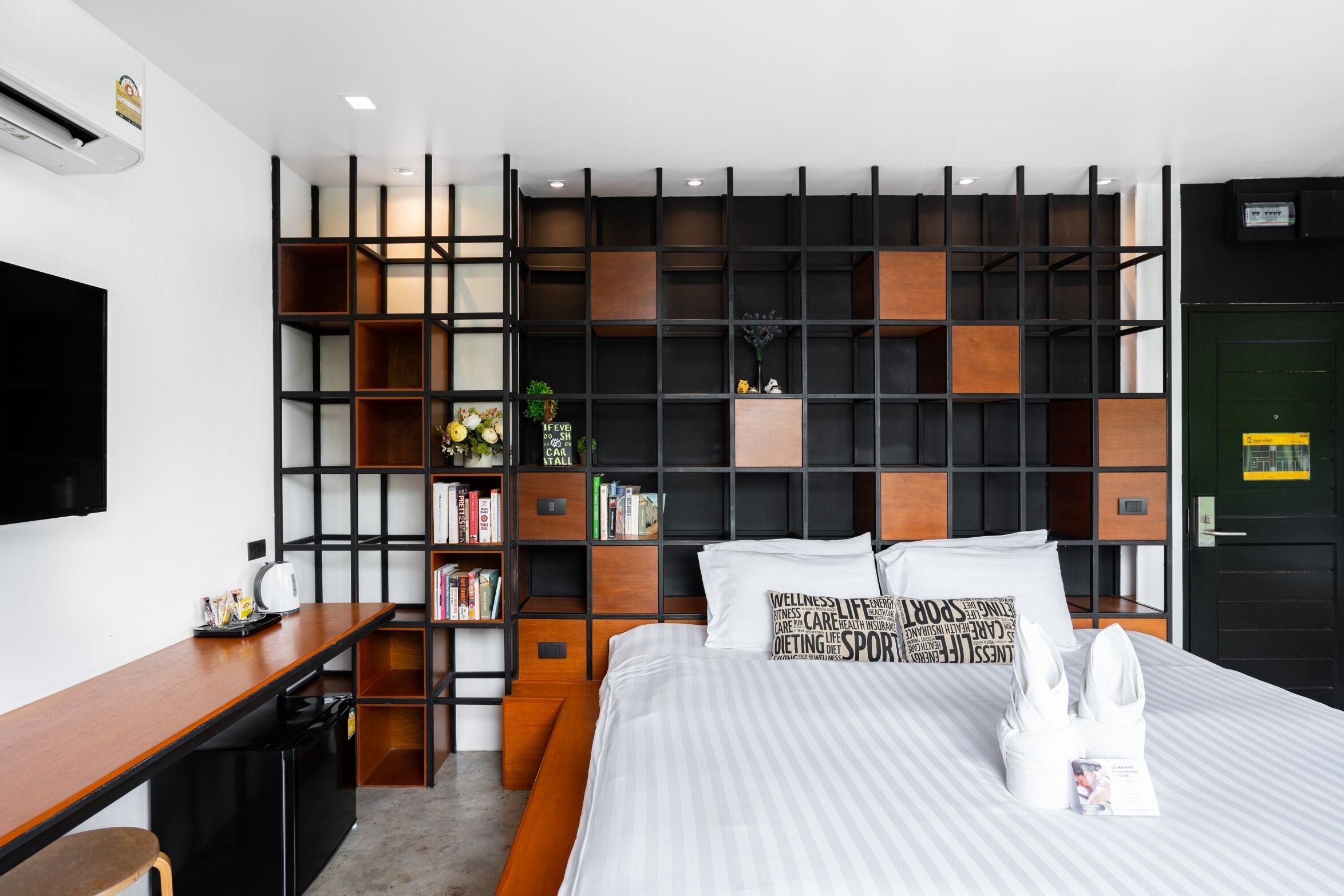 Una habitación de hotel moderna con una cama grande, un escritorio con una silla, una estantería y un televisor.