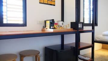A compact room with a kitchenette, a bed, and a window with blinds.