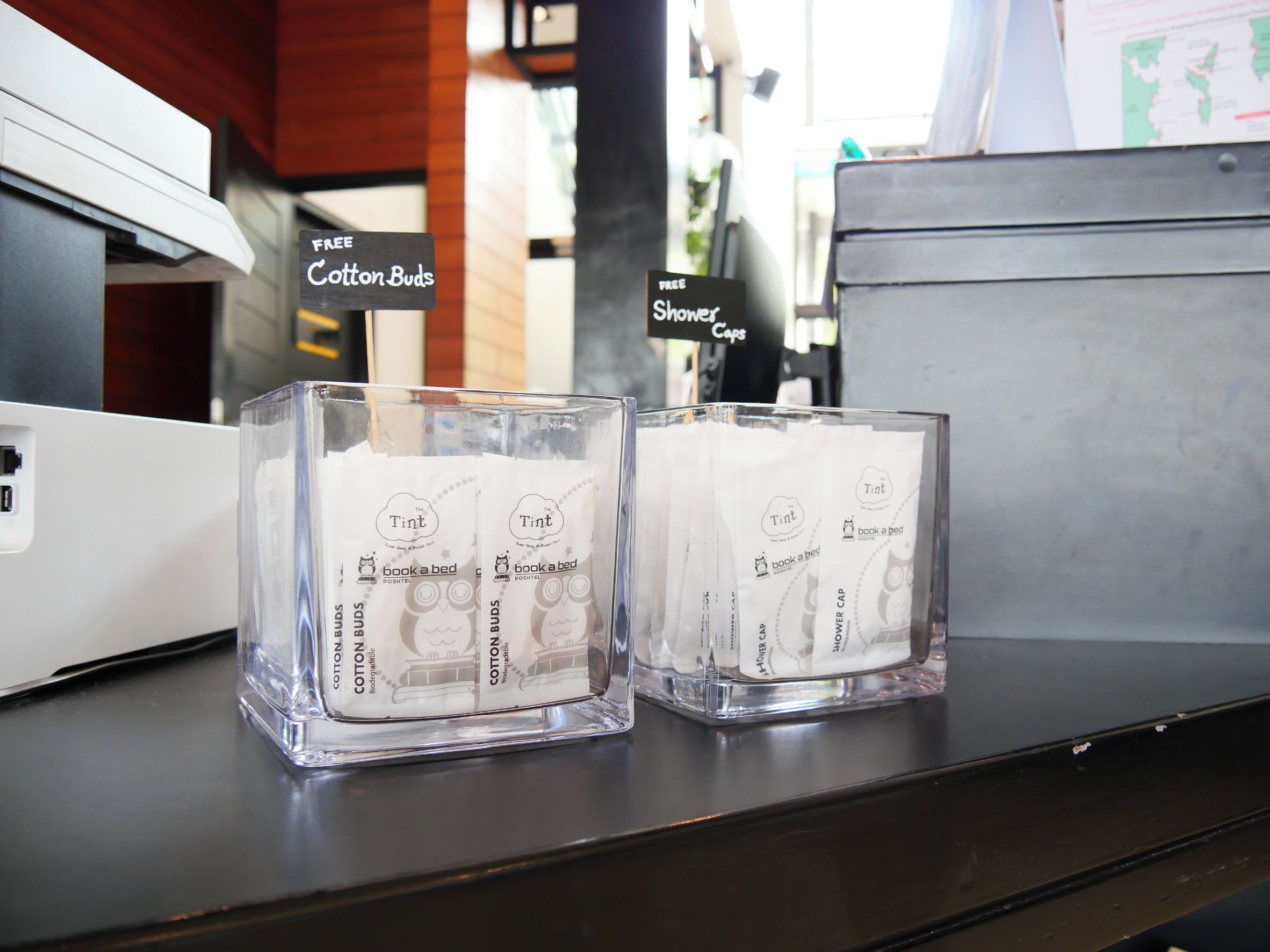 Two glass candle holders with 'The Tint' branding and 'book a bed' text, placed on a dark surface with a white device in the background.
