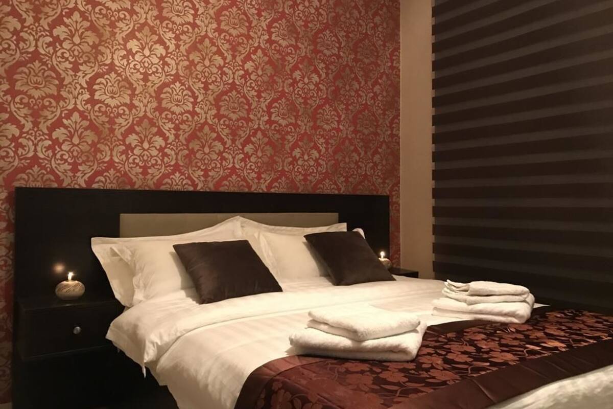 A neatly made bed with white linens and a brown patterned bedspread, a bedside lamp, and a nightstand with a candle.