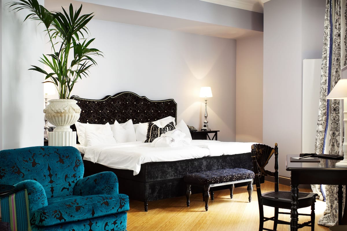 Une chambre d’hôtel avec un grand lit, un fauteuil bleu, une petite table et une plante en pot.