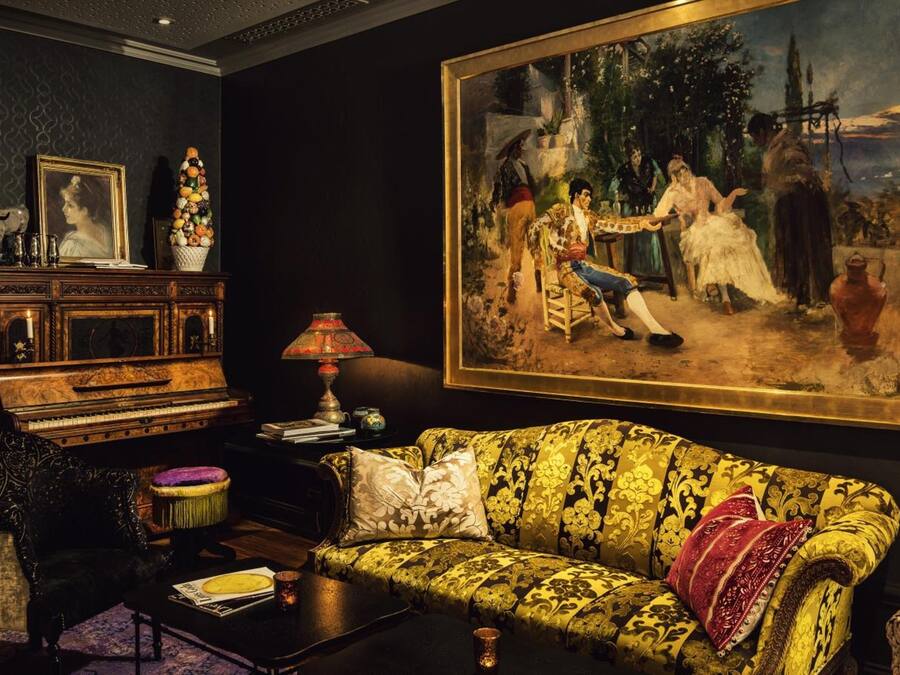 Um quarto com um sofá antigo, um piano, uma pintura grande e um abajur decorativo.