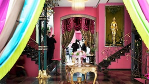 Una imponente escalera con un candelabro, una mesa con arreglos florales y una estatua en una habitación rosa con decoración elaborada.