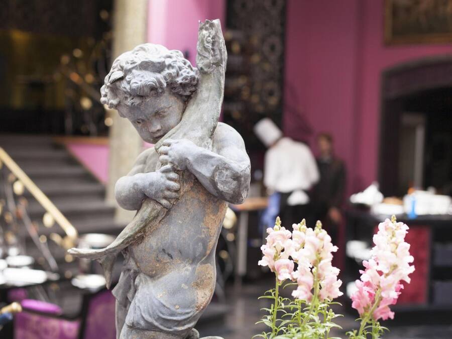 Eine Statue eines Kindes, das einen Vogel hält, in einem Raum mit Treppe und rosafarbenen Wänden.