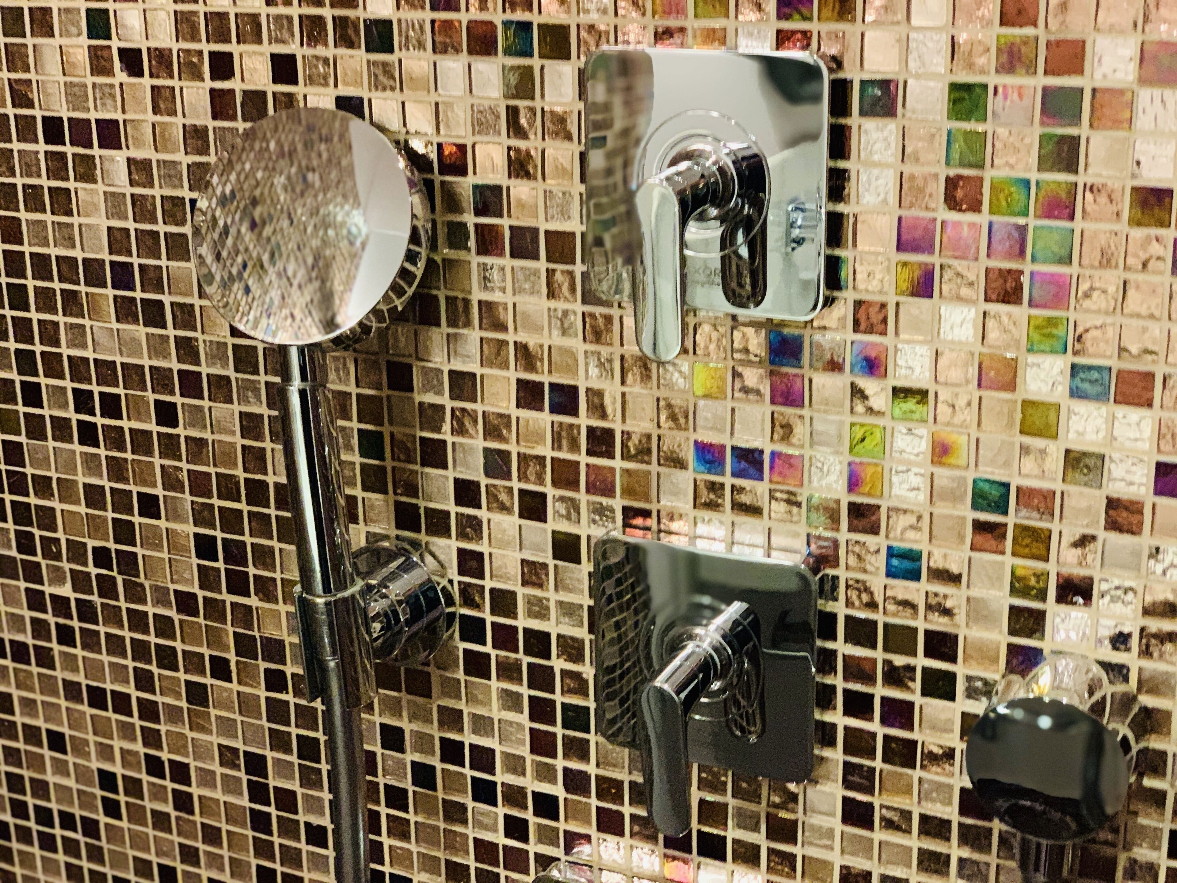 Un espacio de ducha con pared de mosaicos, un cabezal de ducha de mano y una llave instalada en la pared.