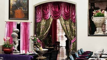 Um interior luxuoso com área de jantar, uma estátua e uma grande janela com cortinas elaboradas.