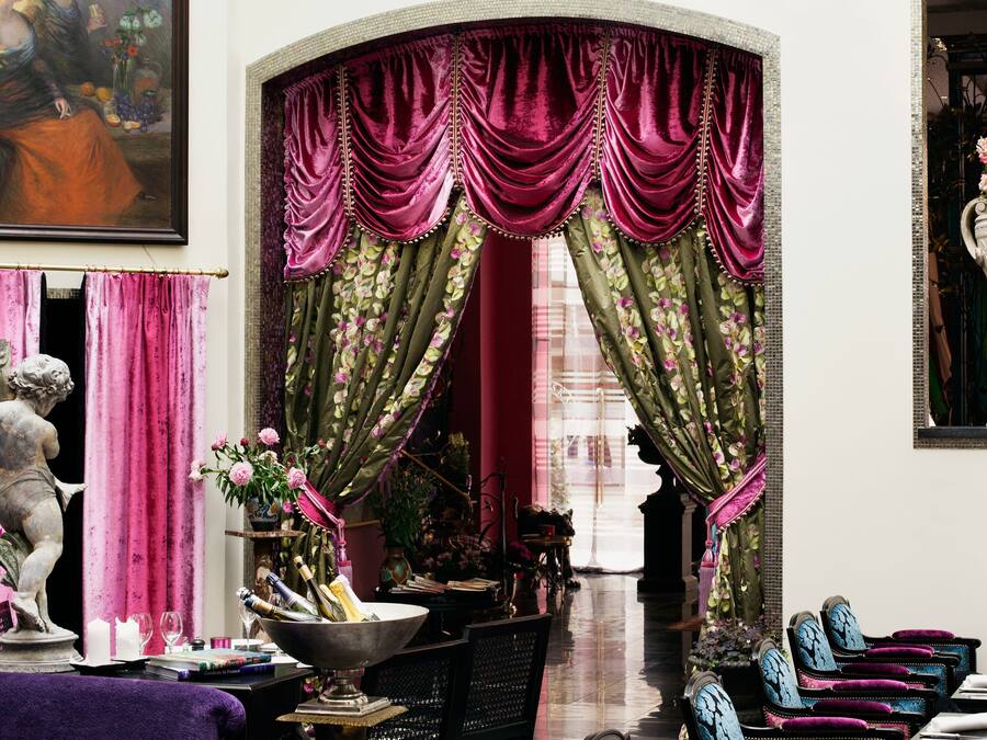Un interior lujoso con comedor, una estatua y un ventanal con cortinas ornamentales.