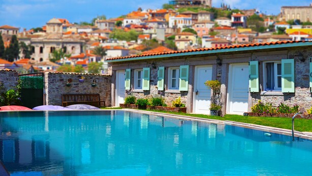 A swimming pool with a stone building in the background. - Cunda Poseidon Hotel (Ayvalik)