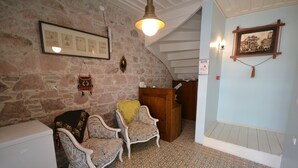 A room with a stone wall, two patterned chairs, a wooden desk, and a patterned floor. - Cunda Poseidon Hotel (Ayvalik)
