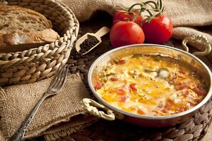 A rustic setting with a bowl of soup, tomatoes, and bread on a woven mat.