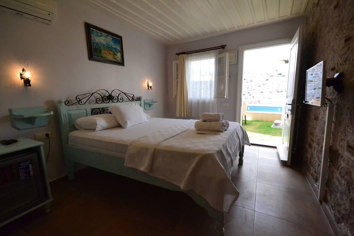 A bedroom with a bed, bedside table, wall-mounted TV, and a view of the outdoors.
