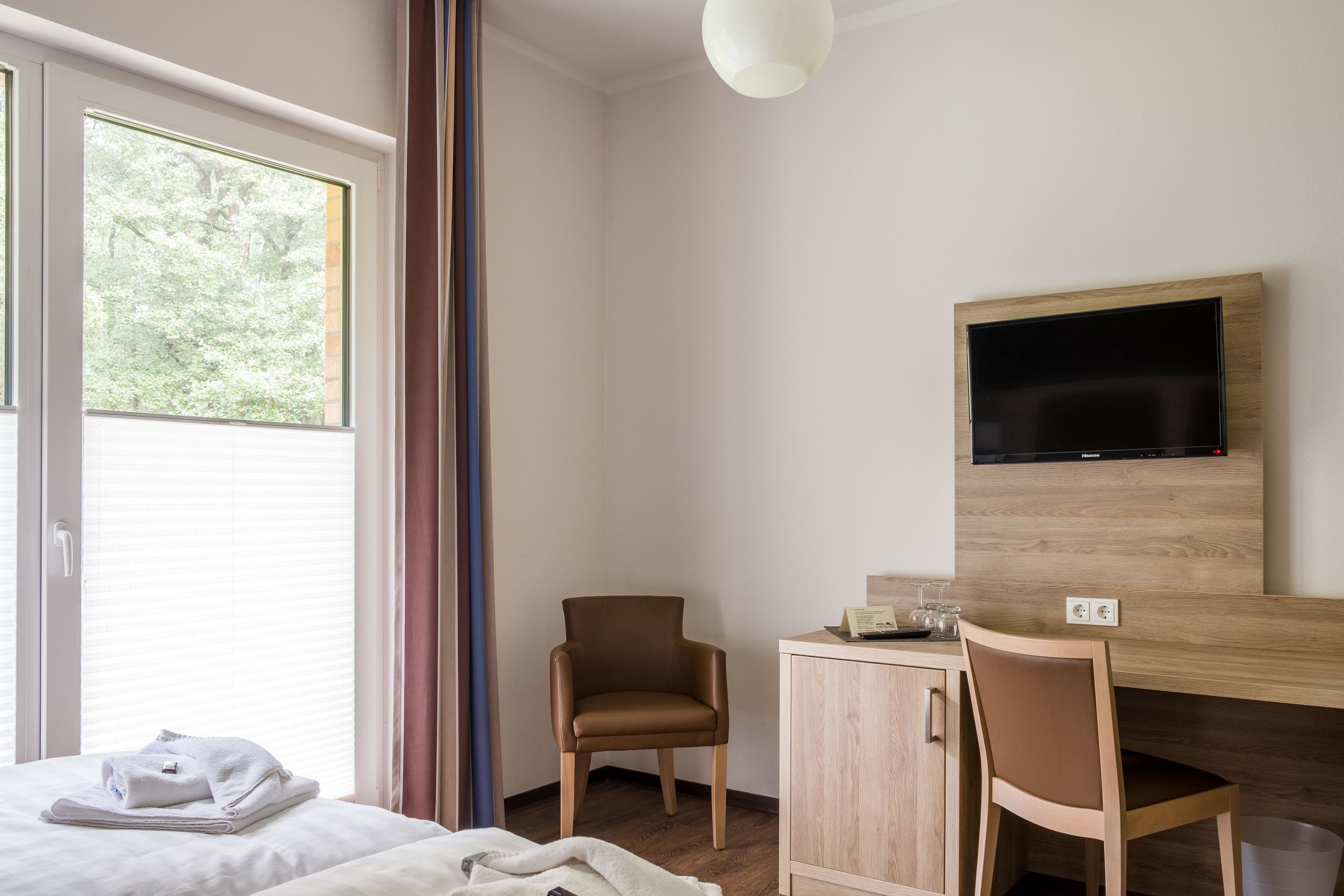 Une chambre d’hôtel comprenant un lit, un bureau avec une chaise, un téléviseur fixé au mur et une fenêtre avec des rideaux.
