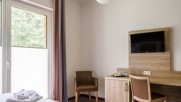 Une chambre d’hôtel comprenant un lit, un bureau avec une chaise, un téléviseur fixé au mur et une fenêtre avec des rideaux.