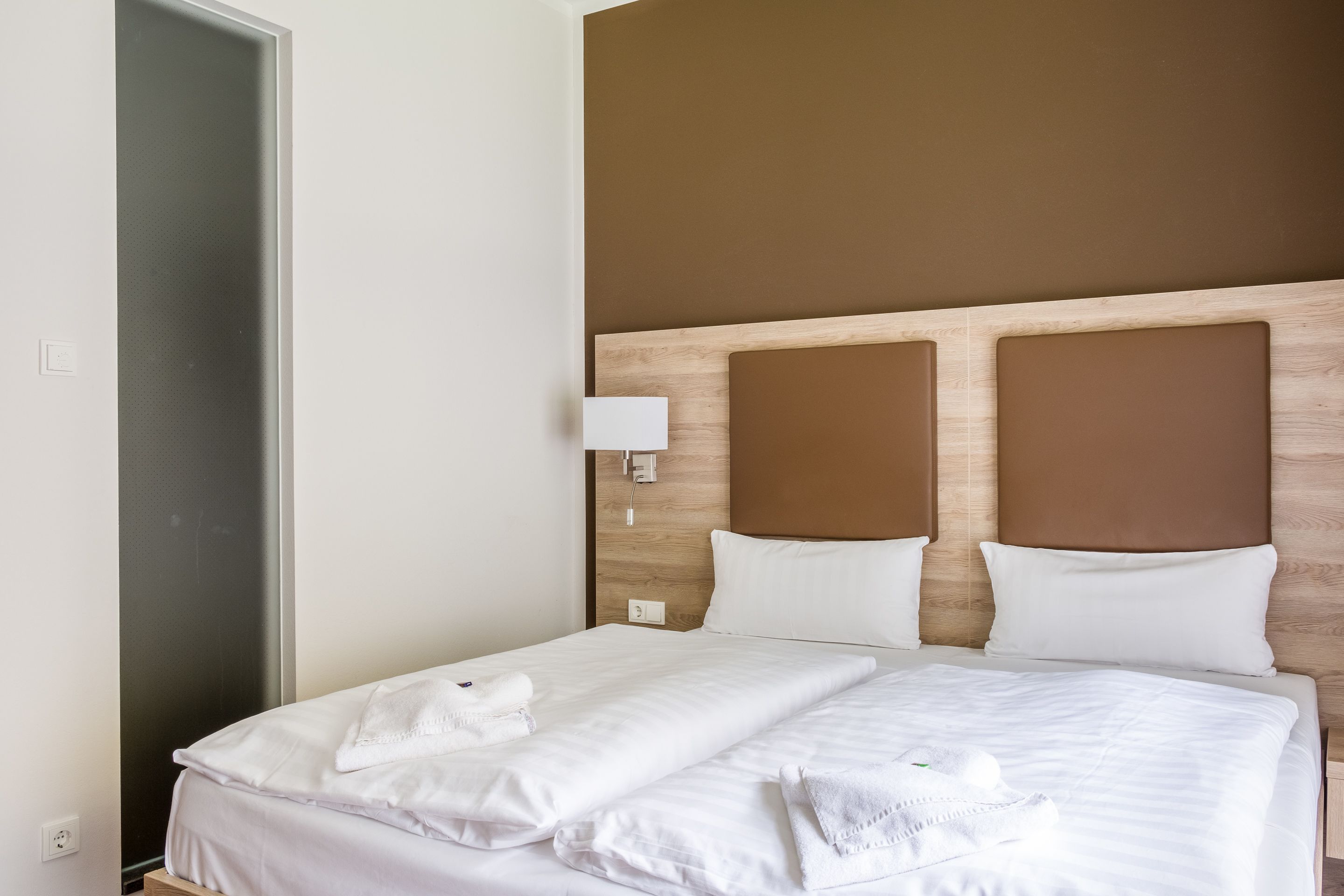 Una camera d'albergo con un letto grande, lenzuola bianche e una testiera in legno.