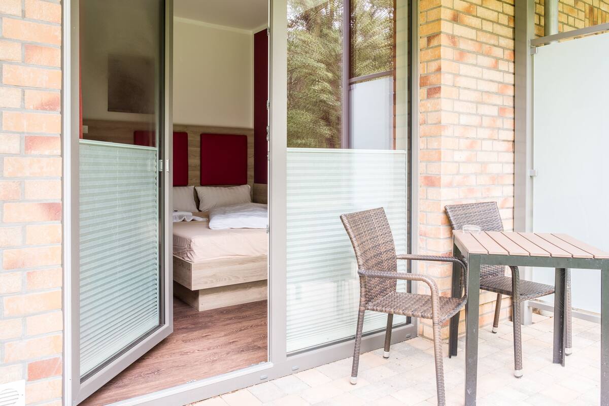 A room with a bed, a sliding glass door leading to an outdoor area with a table and chairs.